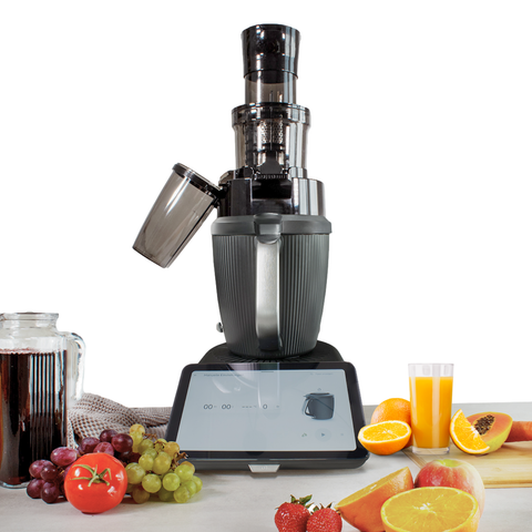 Der dunkelgraue Leckerhelfer SaftPro Entsafter-Aufsatz steht auf dem Display eines Thermomix TM7. Im Vordergrund sind eine Karaffe mit dunklem Saft sowie verschiedene frische Früchte und Gemüse wie Trauben, Orangen, Äpfel und Papaya ausgebreitet.