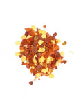 Kleiner Haufen roter geschroteter Chiliflocken und gelber Samen.