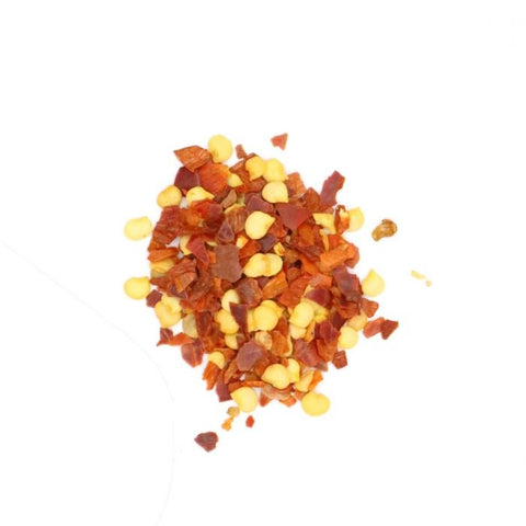 Kleiner Haufen roter geschroteter Chiliflocken und gelber Samen.