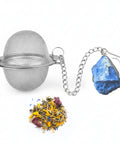 Teesieb aus Metallgeflecht mit einem Lapislazuli-Kristall und losem Kräutertee.