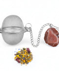 Tee-Ei aus Metallgeflecht mit Kette, rötlich-braunem Kristall und Kräutertee.