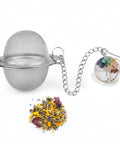 Teesieb aus Metallgeflecht mit einem Chakra-Lebensbaum-Anhänger und losem Tee.