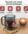 Teesieb mit rotem Achat-Anhänger in einer Glastasse mit Tee neben einer Kerze.