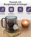 Teesieb mit Bergkristall-Anhänger in einer Glastasse mit Tee, neben einer Kerze.