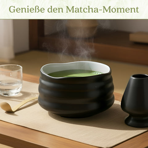 Gewurzladen Nafels Dampfender heißer Matcha Tee in einer schwarzen strukturierten Schale neben einem Besenhalter und Löffel.