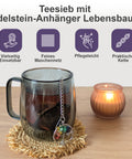 Teesieb mit Edelstein-Lebensbaum-Anhänger in einer Tasse neben einer Kerze.