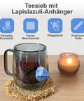 Teesieb mit Lapislazuli-Anhänger in einer Tasse neben einer Kerze.