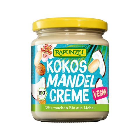 Ein Glas „Rapunzel Kokos Mandel Crème“, ein veganer Bio-Aufstrich mit Kokosnuss- und Mandel-Illustrationen auf einem hellblauen Etikett mit gelbem Deckel.