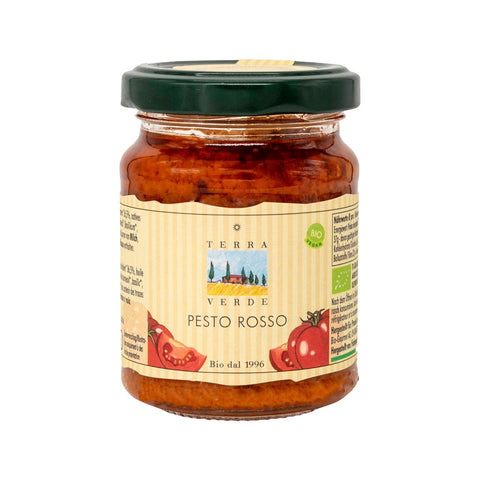 Ein Glas Terra Verde „Pesto Rosso“ mit grünem Deckel. Das Etikett zeigt eine Illustration einer toskanischen Landschaft und frische Tomaten sowie Bio- und Vegan-Siegel.