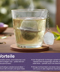 Dampfendes Glas Tee mit einem Netz-Teesieb und Kristall-Anhänger auf einem Untersetzer.