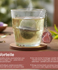 Dampfendes Glas Tee mit einem Netz-Teesieb und rotem Achat-Anhänger auf einem Untersetzer.