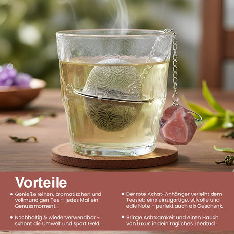 Dampfendes Glas Tee mit einem Netz-Teesieb und rotem Achat-Anhänger auf einem Untersetzer.