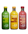 Drei große Glasflaschen „Kloster Kitchen Ingwer Shot“ in den Sorten Classic (grün), Kurkuma (gelb) und Granatapfel (rot), freigestellt vor einem hellgrauen Hintergrund.