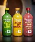 Drei große Glasflaschen „Kloster Kitchen Ingwer Shot“ in den Sorten Classic (grün), Kurkuma (gelb) und Granatapfel (rot), jeweils mit 12 Shots Inhalt und Bio-Siegel.