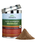 Eine zylindrische Metalldose „Herbaria Waldeslust“ Bio-Gewürz für Pilz- und Wildgerichte, mit leicht geöffnetem Silberdeckel und einem kleinen Häufchen braunem Gewürzpulver daneben.
