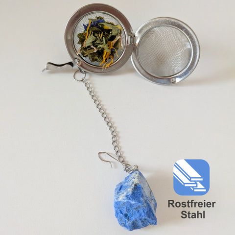 Offenes Teesieb aus Edelstahl mit losem Tee und einem Lapislazuli-Kristall.