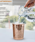 Wasser wird in ein kupfernes Glas mit Blumenmuster gegossen, was eine Spritzbewegung erzeugt.
