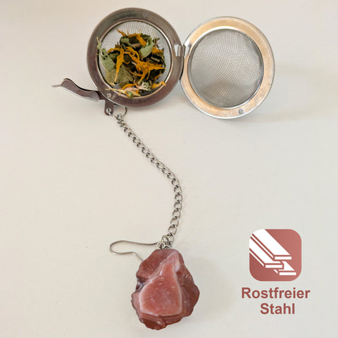 Offenes Teesieb aus Edelstahl mit Kräutertee, verbunden mit einem roten Achat-Stein.
