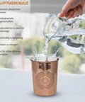 Wasser wird in ein Kupferglas mit Blume des Lebens Design gegossen, was eine Spritzbewegung erzeugt.