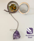 Offenes Teesieb aus Edelstahl mit losem Tee und einem Amethystkristall.