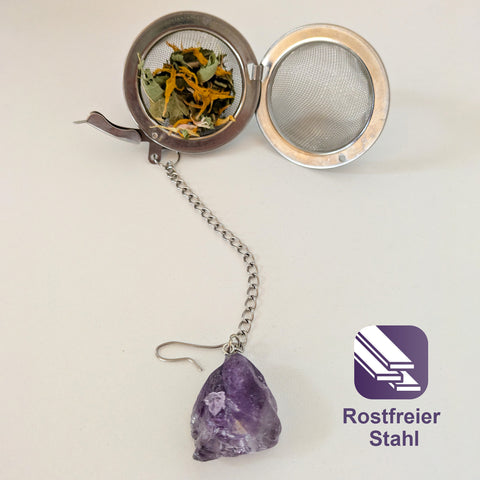 Offenes Teesieb aus Edelstahl mit losem Tee und einem Amethystkristall.