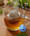 Nahaufnahme einer dampfenden Teetasse mit Sieb und Lapislazuli-Anhänger.