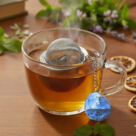 Nahaufnahme einer dampfenden Teetasse mit Sieb und Lapislazuli-Anhänger.