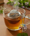 Nahaufnahme einer dampfenden Teetasse mit Sieb und Lebensbaum-Anhänger.