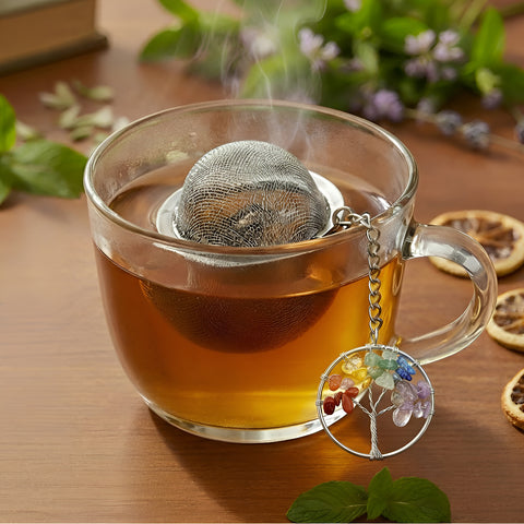 Nahaufnahme einer dampfenden Teetasse mit Sieb und Lebensbaum-Anhänger.