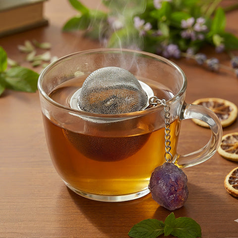 Nahaufnahme einer dampfenden Teetasse mit Sieb und Amethyst-Kristallanhänger.