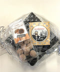 Ein als Geschenk verpacktes Set Glarner Magenträs-Spezialitäten in Klarsichtfolie, bestehend aus Trüffel-Pralinen und Gewürzzucker, verziert mit silbernen und schwarzen Schleifen.