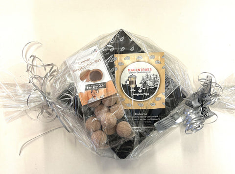 Ein als Geschenk verpacktes Set Glarner Magenträs-Spezialitäten in Klarsichtfolie, bestehend aus Trüffel-Pralinen und Gewürzzucker, verziert mit silbernen und schwarzen Schleifen.