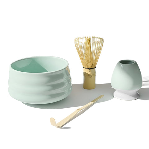 Ein modernes Matcha-Tee-Set bestehend aus einer hellminzgrünen Keramikschale, einem Bambusbesen (Chasen) auf einem passenden Halter und einem Bambuslöffel (Chashaku) auf weißem Hintergrund.