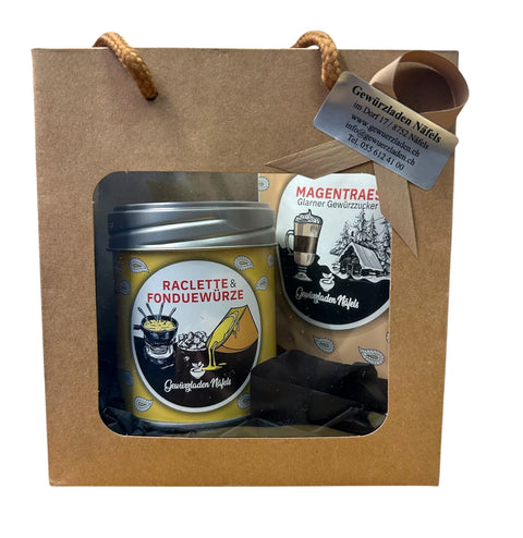 Ein Geschenkkarton vom „Gewürzladen Näfels“ mit einer Dose Raclette- & Fonduewürze und einer Packung Magentraes-Gewürzzucker.