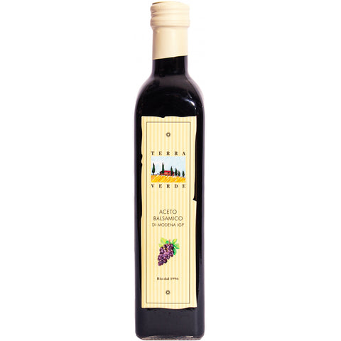 Eine dunkle Glasflasche Terra Verde Aceto Balsamico di Modena IGP, mit einem hellgelben Etikett, das eine Illustration eines Bauernhofs und violetter Trauben zeigt.