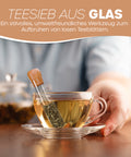 Teefilter aus Glas in Reagenzglasform mit Korken, der lose Teeblätter in einer gefüllten Glastasse aufbrüht.