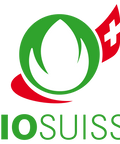 Das offizielle Bio Suisse Logo mit einer stilisierten grünen blattförmigen Knospe in einem Kreis und einem rot-weißen Schweizer Flaggenelement auf der rechten Seite.