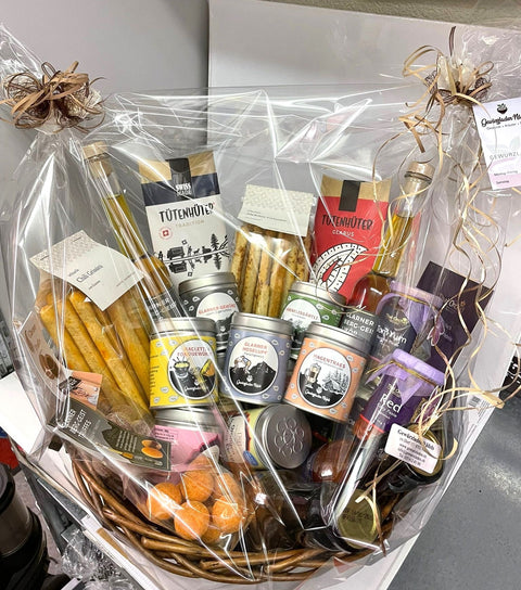 Ein Weidengeschenkkorb in Zellophan, gefüllt mit Schweizer Gourmet-Lebensmitteln.
