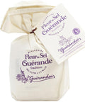 Ein kleiner, cremefarbener Stoffbeutel mit „Fleur de Sel de Guérande“, verziert mit lila Schrift und einem passenden Etikett, das eine traditionelle Salzernte-Illustration zeigt.
