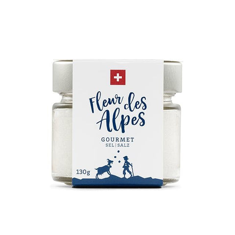 Ein kleines Glas mit 130g „Fleur des Alpes“ Gourmet-Salz, versehen mit einem weißen Etikett mit Schweizer Flagge und einer blauen Illustration einer Person mit einer Bergziege.