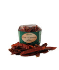Ein Klarsichtbeutel mit „Chili / Cayenne ganz Bizarro“ von Gwürzhüsli, wobei mehrere ganze, getrocknete rote Chilischoten davor auf der weißen Fläche verstreut liegen.