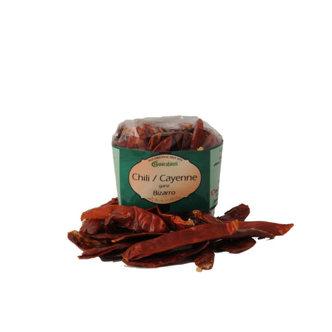 Ein Klarsichtbeutel mit „Chili / Cayenne ganz Bizarro“ von Gwürzhüsli, wobei mehrere ganze, getrocknete rote Chilischoten davor auf der weißen Fläche verstreut liegen.