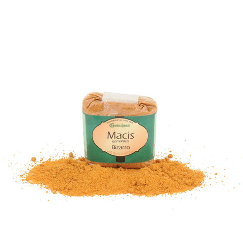 Ein transparenter Kunststoffbeutel mit „Macis gemahlen“ (gemahlene Muskatblüte) von Gwürzhüsli Bizarro, mit einem grün-cremefarbenen Vintage-Etikett, stehend in einem kleinen Haufen aus feinem, orangebraunem Gewürzpulver.