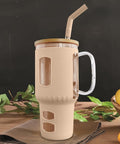 Ein großer, beige-farbener Glasbecher, gefüllt mit einem braunen Getränk, steht auf einem Holztisch mit einer braunen Serviette, grünen Blättern und Zitronen im Hintergrund.