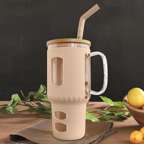 Ein großer, beige-farbener Glasbecher, gefüllt mit einem braunen Getränk, steht auf einem Holztisch mit einer braunen Serviette, grünen Blättern und Zitronen im Hintergrund.