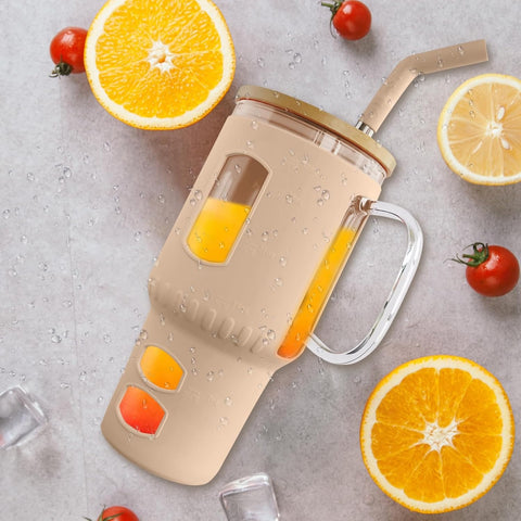 Ein mit Orangensaft gefüllter, beige-farbener Glasbecher mit Henkel und Strohhalm, umgeben von aufgeschnittenen Orangen, Zitronen, Kirschtomaten, Eiswürfeln und Wassertropfen auf einer grauen Oberfläche.