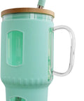 Großer Trinkbecher aus Glas mit mintgrüner Silikonhülle, Holzdeckel, Glasgriff und gebogenem mintgrünem Trinkhalm.