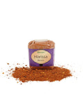 Ein Klarsichtbeutel mit „Harissa Bizarro“ Gewürzpulver der Marke Gwürzhüsli, wobei ein Teil der rötlich-braunen, körnigen Gewürzmischung davor auf der weißen Fläche verstreut liegt.