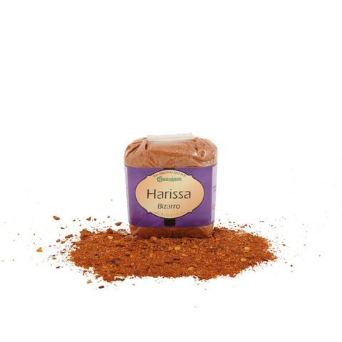 Ein Klarsichtbeutel mit „Harissa Bizarro“ Gewürzpulver der Marke Gwürzhüsli, wobei ein Teil der rötlich-braunen, körnigen Gewürzmischung davor auf der weißen Fläche verstreut liegt.