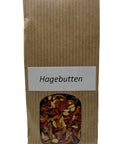 Ein brauner Papierbeutel mit einem kleinen Sichtfenster, das getrocknete orange-rote Hagebuttenschalen und helle Samen zeigt, beschriftet mit einem weißen Etikett „Hagebutten“.